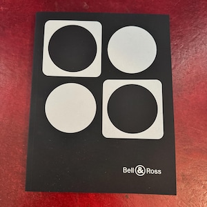 May include: A black rectangular book cover featuring a graphic design of two white circles and two white rounded squares arranged in a grid. The text Bell & Ross is printed in white in the bottom right corner of the black cover surface.