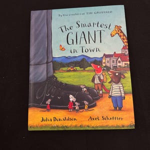 May include: A children's book titled "The Smartest Giant in Town" by Julia Donaldson and Axel Scheffler. The cover features a giant's shoe, cartoon characters, and a giraffe. The book has a blue and orange cover.