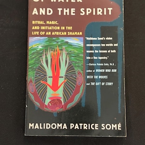 May include: A paperback book titled "Of Water and the Spirit" with the author's name, Malidoma Patrice Somé, at the bottom. The cover features a colorful illustration of a face with a red arrow and green and brown accents. The book's subtitle is "Ritual, Magic, and Initiation in the Life of an African Shaman."