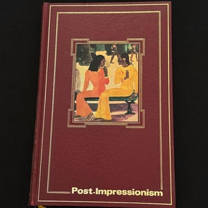 Op de afbeelding: Een bordeauxrood hardcover boek met de titel "Post-Impressionisme". De omslag toont een ingelijste afbeelding van twee figuren in oranje en gele kleding. Gouden randen en letters accentueren de omslag.