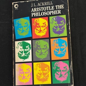 Op de afbeelding: Een vintage paperback boek getiteld "Aristotle the Philosopher" door J.L. Ackrill. De zwarte omslag toont negen kleurrijke vierkanten, elk met een pop-art portret van Aristoteles in verschillende tinten.