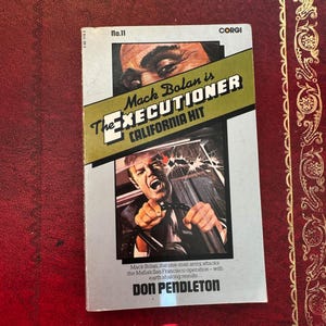 May include: Vintage paperback book titled "Mack Bolan is The Executioner California Hit" by Don Pendleton. The cover features a man in a car and a close-up of a man's face. The book is a Corgi edition.