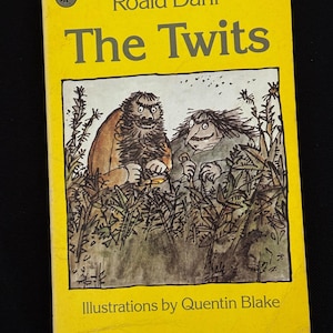 以下が含まれることがあります： ロアルド・ダールの「The Twits」の黄色い本の表紙。クエンティン・ブレイクのイラストで、草むらの中にいる2人のグロテスクなキャラクターが描かれています。タイトルは太字で表示されています。ペンギンのロゴが見えます。