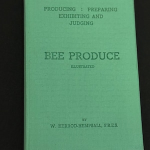 以下が含まれることがあります： 「BEE PRODUCE」というタイトルと「ILLUSTRATED」というサブタイトルが付いた、ヴィンテージの薄緑色の本。表紙には「PRODUCING: PREPARING, EXHIBITING AND JUDGING」とも書かれています。著者の名前、W. Herrod-Hempsall, F.R.E.S.が下部に印刷されています。