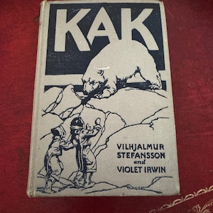 Puede incluir: Libro antiguo titulado "KAK" con una ilustración en blanco y negro de un oso polar en la portada. La portada también presenta ilustraciones de niños y los nombres de los autores: Vilhjalmur Stefansson y Violet Irwin.