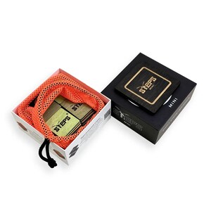 Può includere: Un set di blocchi di legno con la scritta "STEPS MINI" in una scatola bianca con un sacchetto a rete arancione. I blocchi sono in una scatola nera con lo stesso testo. I blocchi sono marrone chiaro e verdi.