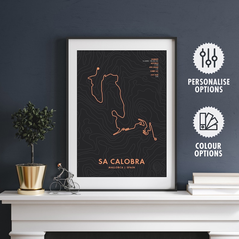 May include: A black and white topographic map print of the Sa Calobra cycling route in Mallorca, Spain. The route is highlighted in orange. The print is framed in a white frame.