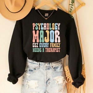 May include: Black sweatshirt with the text "Psychology Major Cuz Every Family Needs A Therapist" in colourful retro font.