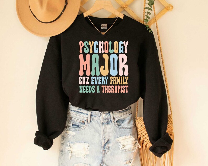May include: Black sweatshirt with the text "Psychology Major Cuz Every Family Needs A Therapist" in colourful retro font.