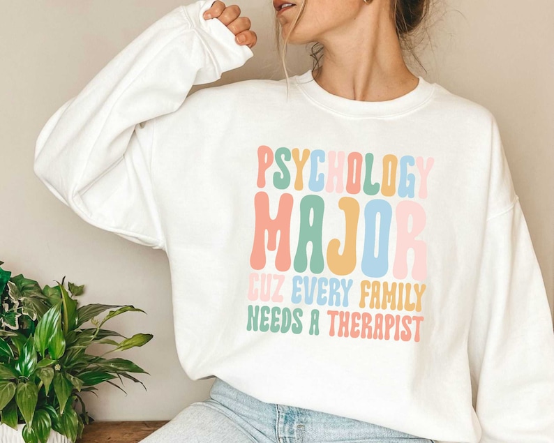 May include: White sweatshirt with the text "Psychology Major Cuz Every Family Needs A Therapist" in rainbow colours.