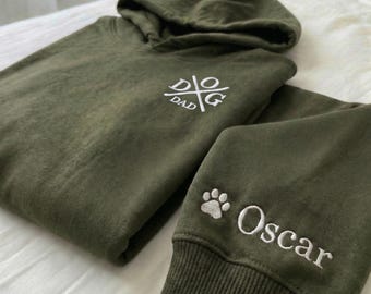 Könnte beinhalten: Olivgrünes Hoodie und passende Jogginghose. Das Hoodie hat den weißen Text "DOG DAD", einen Pfotenabdruck und den Namen "Oscar" auf dem Ärmel gestickt. Das Set ist aus einem weichen Material gefertigt.