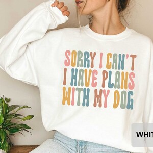 May include: White sweatshirt with the text "Sorry I can't I have plans with my dog" in colorful, wavy letters.
