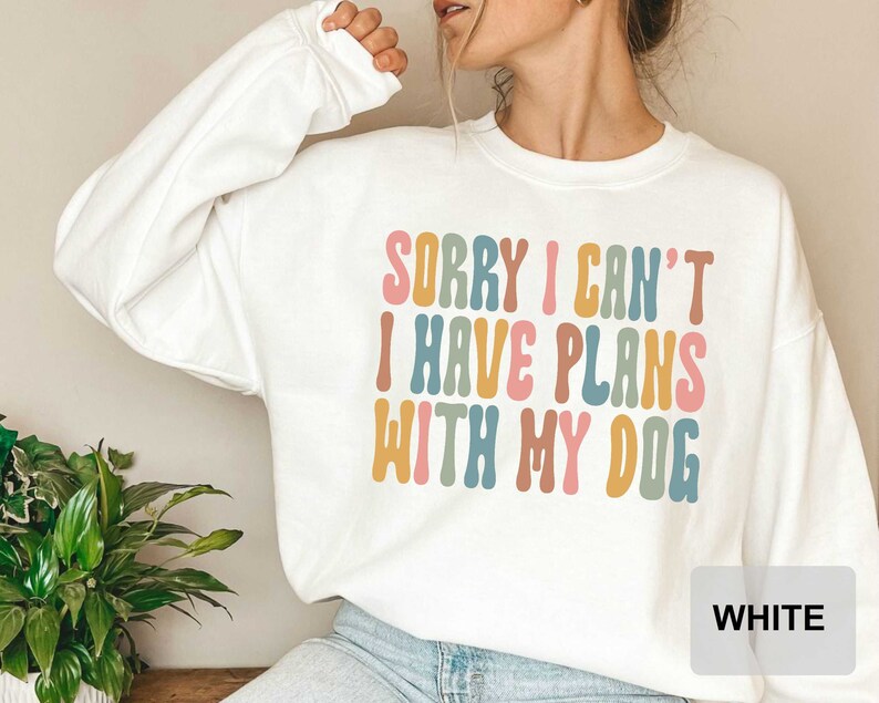 May include: White sweatshirt with the text "Sorry I can't I have plans with my dog" in colorful, wavy letters.
