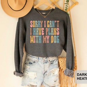 May include: Dark heather grey sweatshirt with the text "Sorry I can't I have plans with my dog" in rainbow colors.