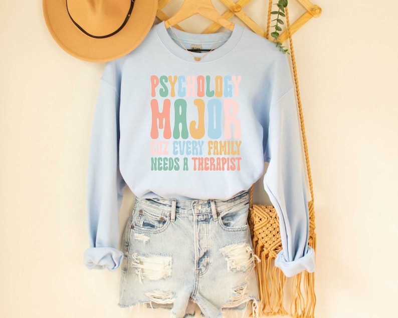 May include: Light blue sweatshirt with the text "Psychology Major cuz every family needs a therapist" in rainbow colours.