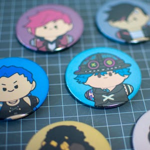 May include: Five round button badges featuring cartoon characters. The badges are colourful and feature different characters with unique designs.