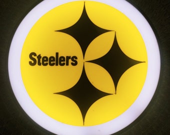 May include: A yellow circle with a black Steelers logo in the center. The logo features two intersecting black diamonds.