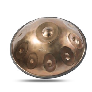 May include: A bronze-colored handpan drum with a black rubber rim. The instrument has multiple circular indentations of varying sizes across its surface. The brand name "SHANIPAN" is visible on the lower part of the drum.