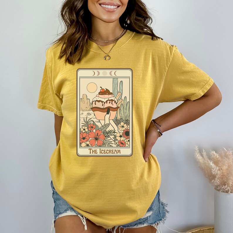 May include: A yellow t-shirt with a graphic of a cartoon ice cream cone with a cherry on top. The ice cream cone is walking on two legs and is surrounded by flowers and cacti. The text "The Ice Cream" is printed below the image.