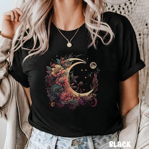 May include: Black t-shirt featuring a crescent moon graphic surrounded by colourful flowers. The moon is yellow and the flowers are pink, purple, and green.