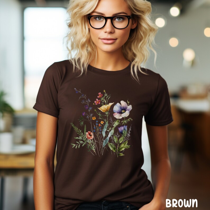 Op de afbeelding: Een bruin t-shirt met een bloemenprint met verschillende bloemen in tinten roze, paars, geel en blauw.