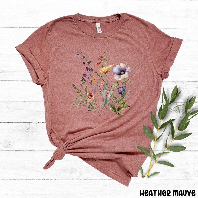 Op de afbeelding: Een heide-paarse t-shirt met een aquarel bloemenprint met verschillende bloemen in tinten roze, paars, geel en oranje.
