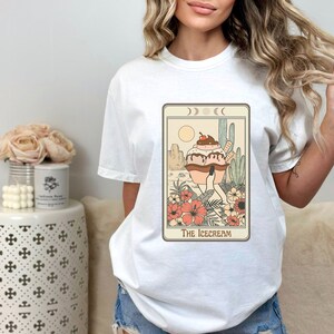 May include: White t-shirt with a graphic of a tarot card featuring an ice cream cone with a cherry on top. The card is titled "The Icecream".