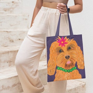 Könnte beinhalten: Eine marineblaue Tragetasche mit einer detaillierten Illustration eines goldfarbenen Hundes mit einer rosa Blume und einer grünen Perlenkette. Der Hund hat die Zunge herausgestreckt. Die Tasche hat marineblaue Griffe.