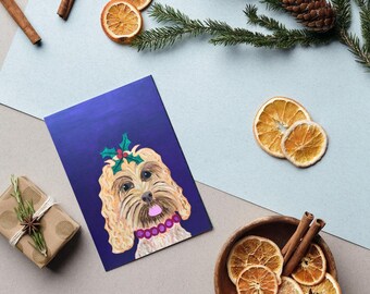 May include: A greeting card with a painted illustration of a dog wearing a holly headpiece, set against a deep blue background. The image is surrounded by dried orange slices, cinnamon sticks, and a wrapped gift, suggesting a holiday theme.