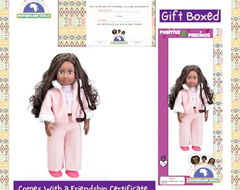 Puede incluir: Una muñeca rosa y blanca con cabello castaño y ojos marrones. La muñeca lleva una chaqueta rosa con cuello de piel blanca y pantalones rosas. La muñeca sostiene un certificado que dice "Certificado de Amistad". La muñeca viene en una caja de regalo con las palabras "Caja de regalo" y "Positivo & Preciado" en ella.