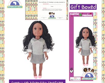 Op de afbeelding: Een bruine pop met krullend zwart haar, die een zwart-wit gestreepte jurk met een grijs vest draagt. De pop houdt een vriendschapscertificaat vast. De pop wordt in een cadeaudoos geleverd en wordt geleverd met een vriendschapscertificaat.