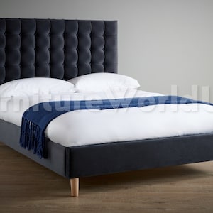 May include: A dark blue upholstered bed frame with a tufted headboard and wooden legs. The bed is made with white bedding and a blue throw blanket.