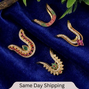 May include: Four gold-coloured, curved jewellery pieces with embedded gemstones. The pieces feature red, green, and clear stones. The jewellery is displayed on a dark blue velvet surface. The text "Same Day Shipping" is at the bottom.