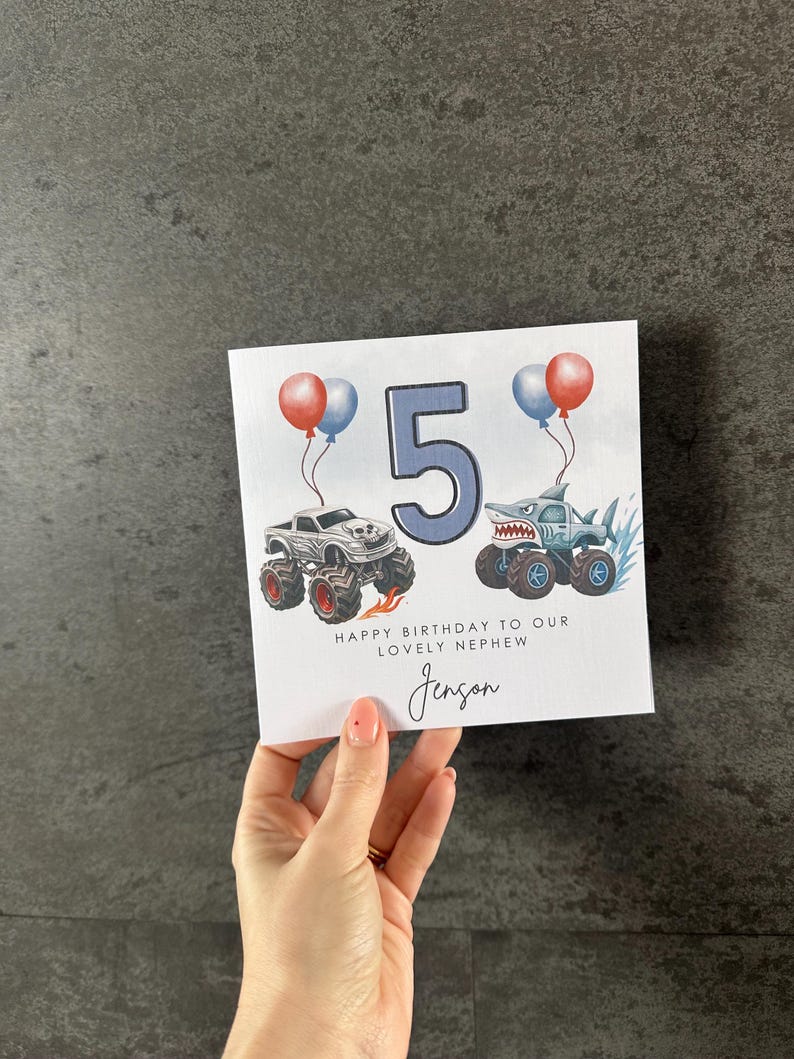 May include: A birthday card featuring the number 5 in blue, two monster trucks, and balloons. The card says "Happy Birthday to our lovely nephew Jenson."