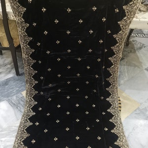 May include: A black velvet shawl with detailed gold embroidery along the borders and across the fabric. The shawl is rectangular and is displayed, highlighting the ornate design and luxurious texture of the material.