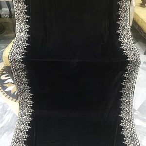 May include: A black velvet shawl with a white embroidered border. The embroidery features a floral design.