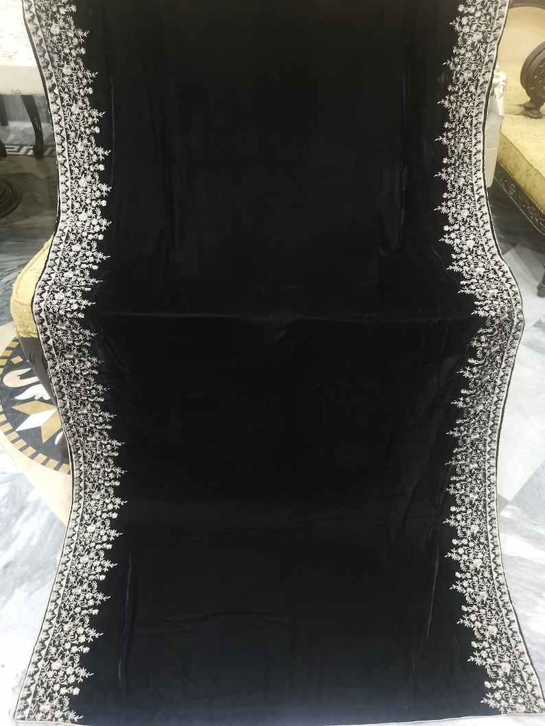 May include: A black velvet shawl with a white embroidered border. The embroidery features a floral design.