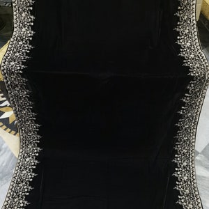 May include: A black velvet shawl with a white embroidered border. The embroidery features a floral design.