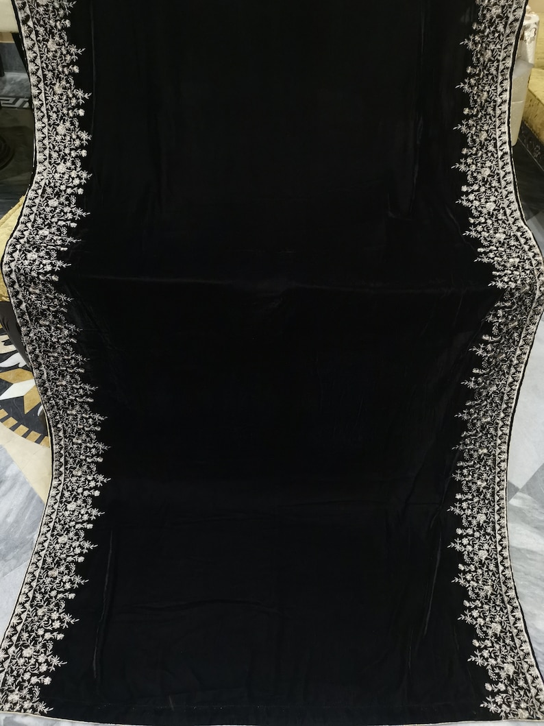 May include: A black velvet shawl with a white embroidered border. The embroidery features a floral design.