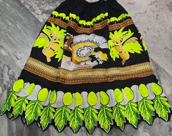 May include: Black skirt with neon green and yellow embroidery. The skirt has a detailed design featuring palm trees, a central figure, and leaf patterns along the hem. The design includes brown and white accents.