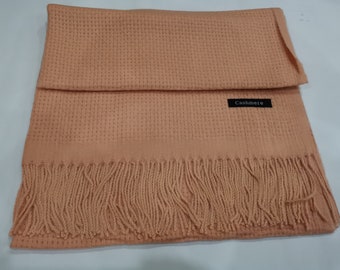 May include: A peach-coloured cashmere scarf with a waffle knit texture and fringe trim. The scarf has a black label that says "Cashmere".