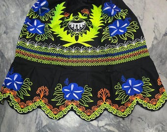 May include: Black skirt with colourful floral embroidery. The skirt features blue and white flowers, neon green leaves, and orange accents. The hemline has a scalloped edge, and the design includes a central emblem.