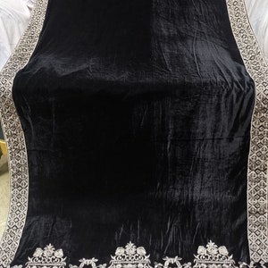 May include: A black velvet shawl with a silver embroidered border. The border features a repeating geometric pattern and a floral design at the bottom.