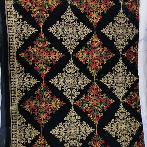 May include: Black velvet fabric with intricate gold embroidery featuring a repeating floral pattern. The embroidery includes red, green, and yellow accents.