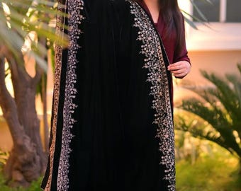 May include: A black velvet shawl with a silver embroidered border. The shawl is draped over a person's shoulders and is worn with a maroon dress.