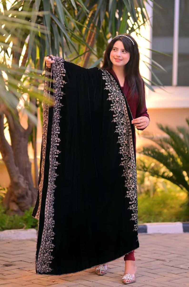 May include: A black velvet shawl with a silver embroidered border. The shawl is draped over a person's shoulders and is worn with a maroon dress.