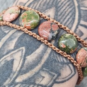 May include: A bracelet with a copper cord and round, multi-colored stones. The stones are a mix of green, pink, and brown.