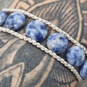 May include: A white cord bracelet with blue and white patterned stones. The bracelet is made with a macrame knot design.