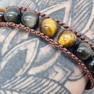 May include: A brown braided cord bracelet with alternating gold tiger's eye and black obsidian beads.