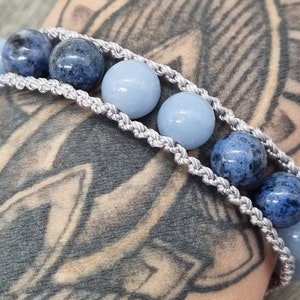 May include: A macrame bracelet featuring alternating light blue and dark blue spherical beads. The bracelet is made with a light gray woven cord. The beads are approximately 1 cm in diameter.